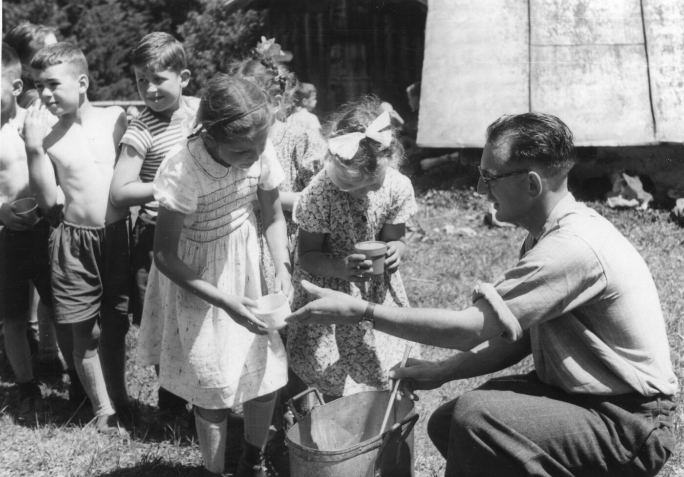 Durstig nach der Wanderung: Lehrer Lorenz Zinsli mit Kindern beim Anstehen für ein Getränk anlässlich der Maiensässfahrt im Jahr 1950. Die Tradition der Maiensässfahrt gibt es seit dem Jahr 1854.