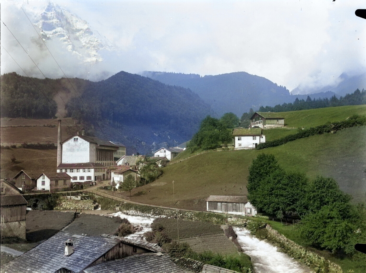 Alte Dorfansicht von Riedern mit dem Löntsch: Die Leiche von Andreas Stüssi wird beim Wehr der Bleicherei angespült, dem grossen Fabrikgebäude links mit dem Kamin. Das Bild ist digital nachkoloriert. 